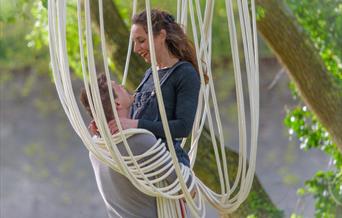 A man and woman in a romantic pose in a rope chair hanging from a tree