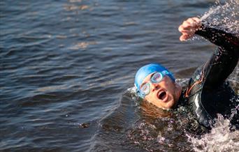 A swimmer in blue swim hat and goggles swimming crawl