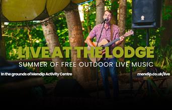 Sam Evans (musican) playing on guitar and singing into microphone. Mendip Lodge logo. Text promotes Live at the Lodge: Summer of free outdoor live mus