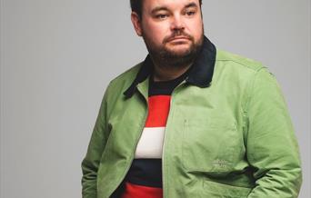 Lloyd sitting on a stool wearing a green bomber jacket