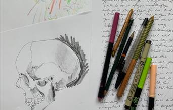 A sketch of a skull, next to some hand-written writing and a selection of stationery