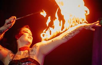 A circus performer with a fire stick and fire on her arm