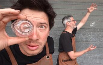 One man looking through glass and another juggling a glass