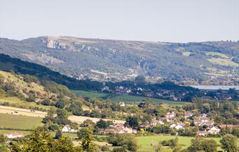 View across fields to a village, lake and rocky hills in the background