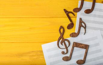 Two sheets of music on a wooden surface with some clefs and musical notes