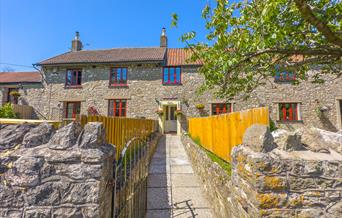 Exterior image of a fenced path leading towards the stone buildings of Norton Court Farm self-catering holiday cottages near Weston-super-Mare