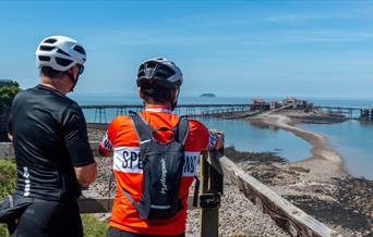 Two cyclists leaning against a fence admiring a sea view