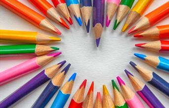 An arrangement of brightly coloured pencils creating a white heart shape in the middle