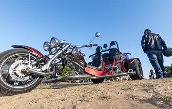 A leather clad biker walks past a motor trike