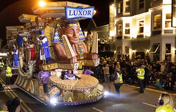 A massive Egyptian-themed huge brightly-coloured carnival float which is as tall as the buildings it is passing.