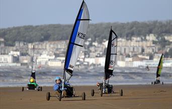 Four Blo-karts or land yachts racing along a sandy beach