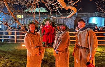 A night time Wassail ceremony featuring four men in traditional dress and someone sitting on a swing