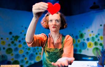 Bright photograph of an actor holding a felt red heart.