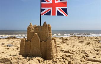 Sandcastle on a beach with a Union Jack flag on top