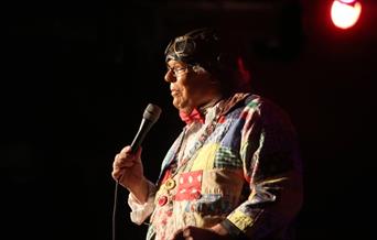 Roy Brown on stage holding a microphone with a spot light on him.