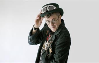 Joe Pasquale staing at the camera with a green suit and a light grey background.