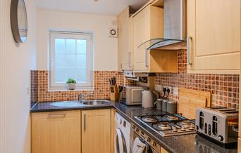 Kitchen inside the Seaside Apartments Weston-super-Mare featuring wooden units, appliances, tiles and a dark worktop