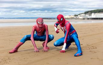 Two characters dressed as Spiderman in a crouched down Spiderman pose on Weston-super-Mare beach