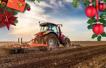 Image of a red tractor and machinery working on a ploughed field with festive items at the top of the picture