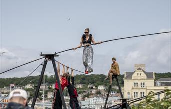 A trapeze artist walking on a tightrope and holding a large pole for balance