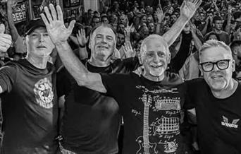 Black and white photo of four band members waving at the camera with a large crowd behind