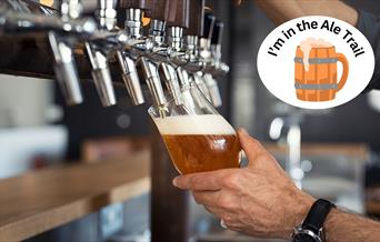 A hand tilting a glass and filling it with beer at the pump