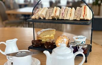 Traditional afternoon tea with pot of tea and cake stand with cakes and sandwiches