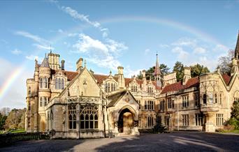 Exterior view of a large turreted mansion with a rainbow above