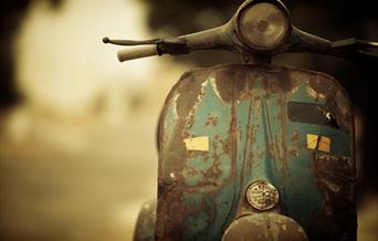 Front view of a rusty green Vespa-style scooter