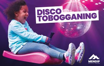 Little girl looking happy and excited riding a zibob toboggan. Background display a disco ball on a purple background, with light glowing down onto th