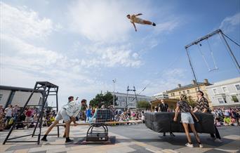 An acrobat high in the blue sky above the crowds and some apparatus