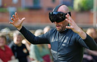 A man all in black wearing a huge black goggle headset on his face