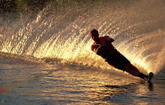 Silhouette of a water skiier with the golden glow of the wash behind him at sunset