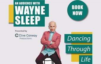 Wayne Sleep in pink jacket sitting on a barstool