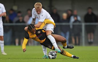 A Newport County footballer about to fall to the ground as he's tackled by a Weston-super-Mare footballer