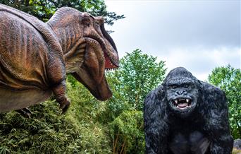 An animatronic dinosaur at Wookey Hole staring at a giant model gorilla