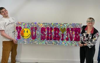 A photo including Megan Clark-Bagnall holding a banner with the words 'YOU SHRINE'