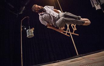 Man floats in air on a chair, dark surrounding