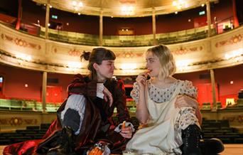 2 female performers sat on stage eating