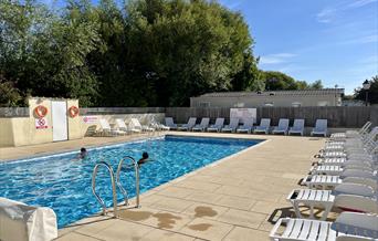 Outdoor swimming pool on a sunny day with two people swimming and lots of empty sun loungers