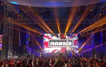 A crowd of people with hands raised facing Noasis