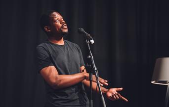 Saili Katebe talking into a microphone with a black curtain behind him.