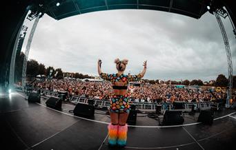 A brightly dressed performer on stage in front of a huge crowd