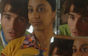 heads and shoulders of a young couple looking into mirrors so that you can see them reflected back. White male with a green jumper and and Asian femal