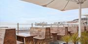 Wooden outside seating area looking out to sea with plants and under a large umbrella