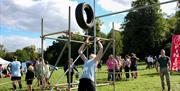 A sports competitor throwing a large tyre up into the air and over a scaffold frame