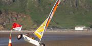 A white land yacht with a yellow, orange and white sail goes around the red and white marker flag on two wheels at Brean Beach Somerset