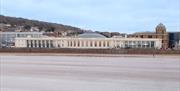 Picture taken from a sandy beach looking towards a long one-storey building with a circular ballroom in the middle