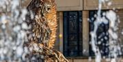 A golden angel-shaped statue photographed between white jets of water