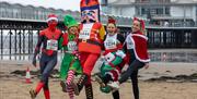 Four runners in festive fancy dress put their best foot forward on the beach in front of the Grand Pier, Weston-super-Mare ahead of the town's annual